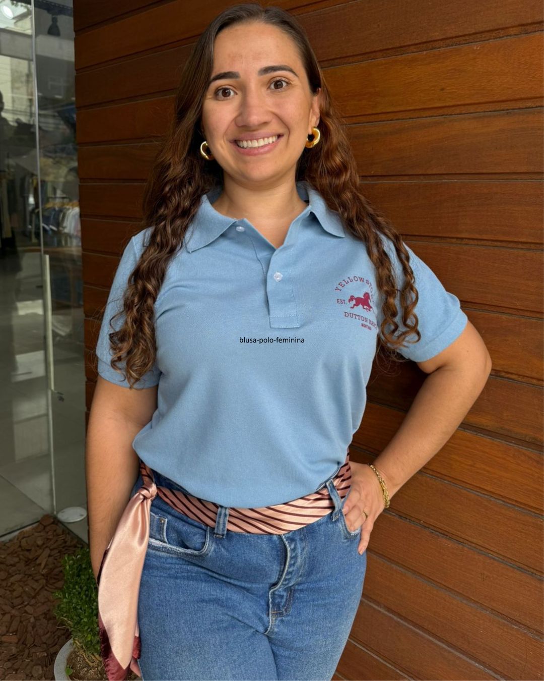 mulher-usando-blusa-polo-feminina-azul-com-estampa-no-peito-em-frente-a-parede-de-madeira