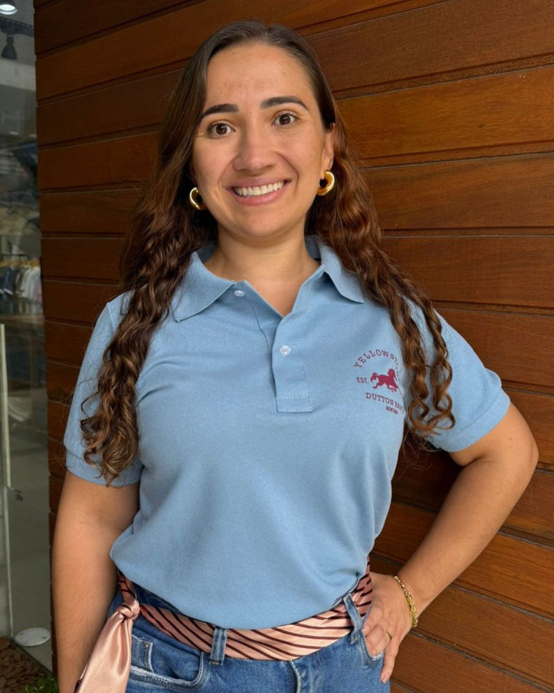mulher-usando-blusa-polo-feminina-azul-com-estampa-no-peito-em-frente-a-parede-de-madeira