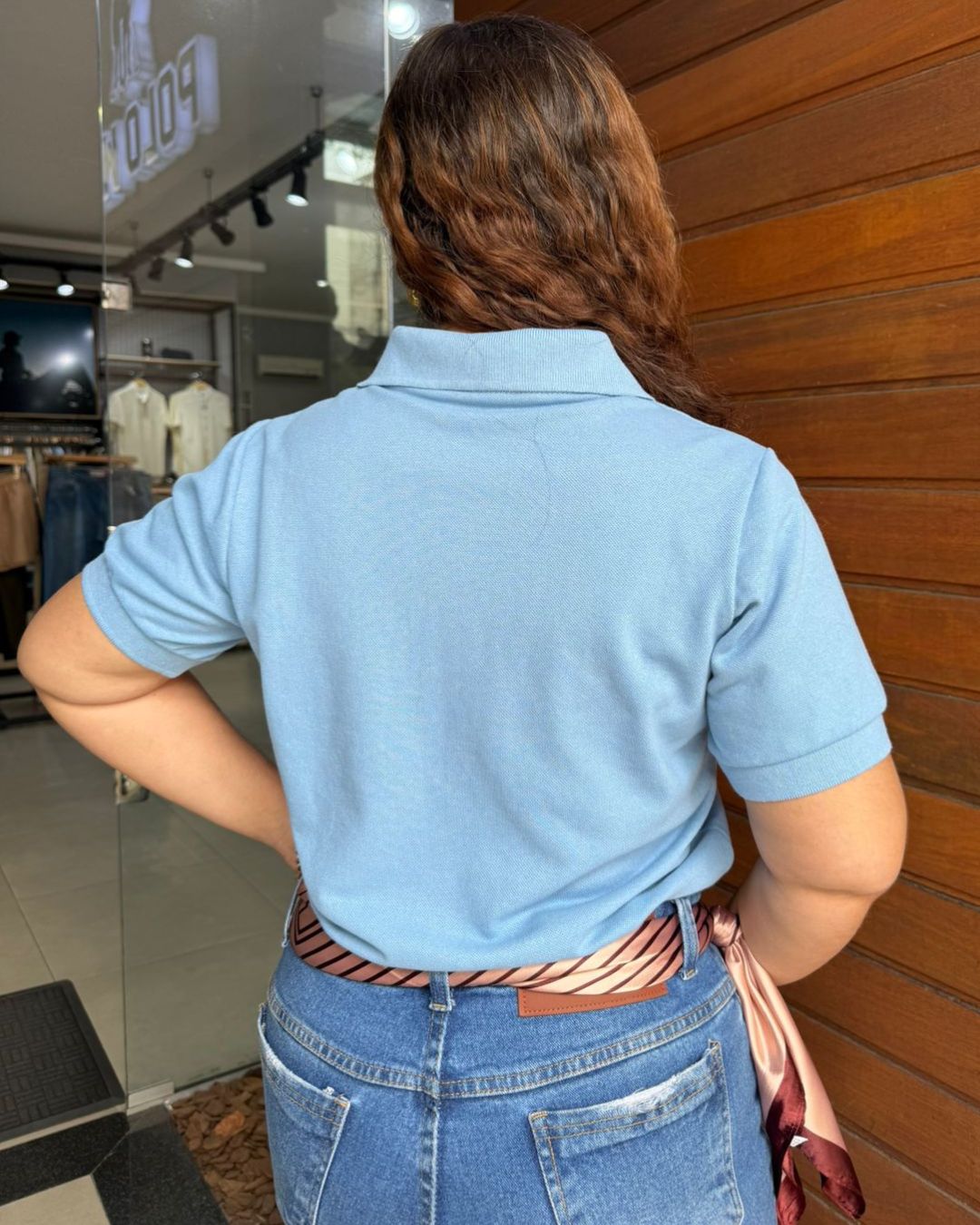 mulher-usando-blusa-polo-feminina-azul-com-estampa-no-peito-em-frente-a-parede-de-madeira-costas