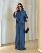 Modelo usando conjunto all jeans azul: blusa com manga balonê e botões frontais, calça pantalona longa com elástico na cintura.