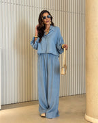 Modelo usando conjunto all jeans azul: blusa com manga balonê e botões frontais, calça pantalona longa com elástico na cintura.