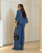 Modelo usando conjunto all jeans azul: blusa com manga balonê e botões frontais, calça pantalona longa com elástico na cintura.