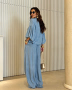 Modelo usando conjunto all jeans azul: blusa com manga balonê e botões frontais, calça pantalona longa com elástico na cintura.